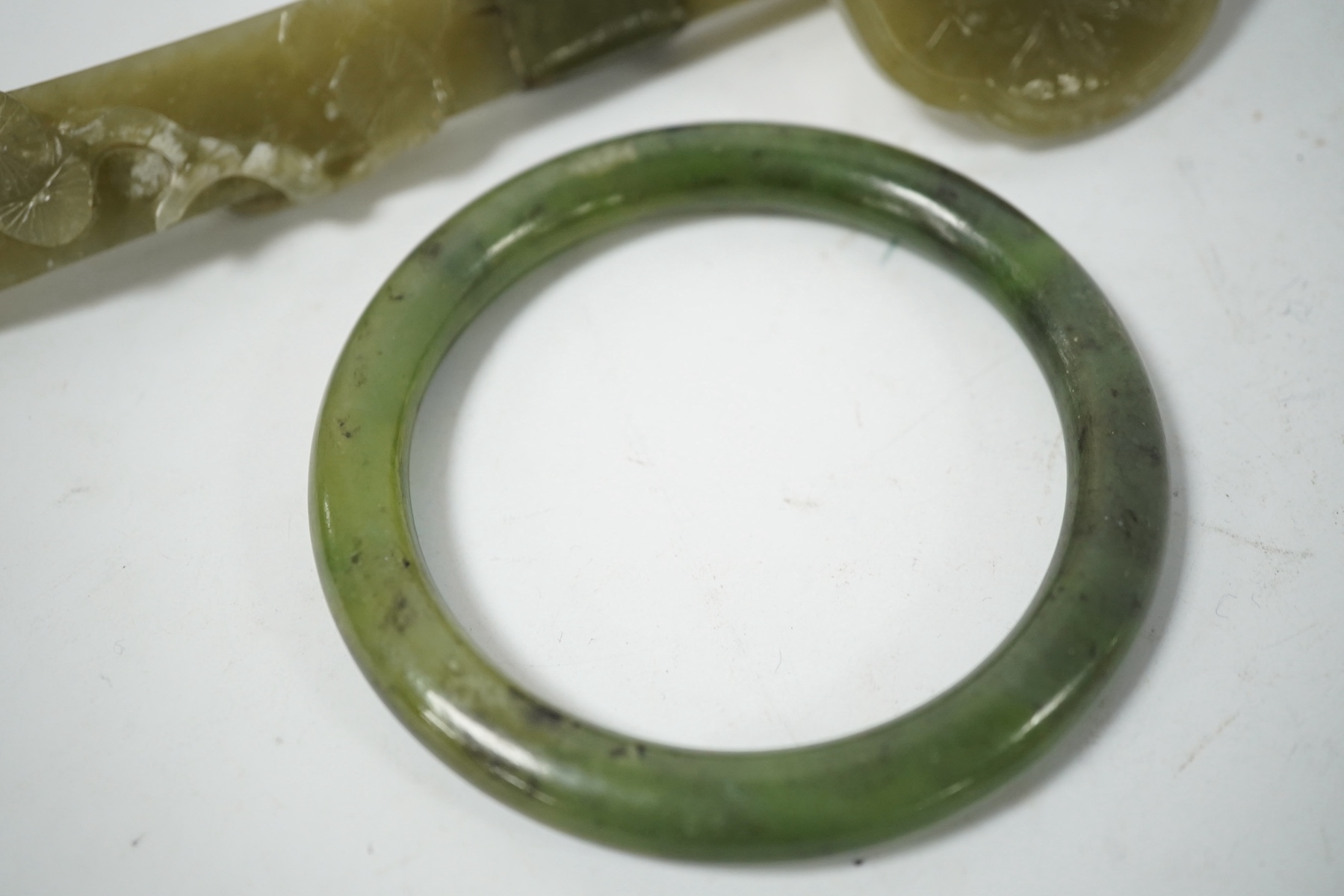 A Chinese celadon jade ruyi sceptre (incomplete) and a spinach jade bangle, late Qing, largest 15.5cm in length (2). Condition - bangle good